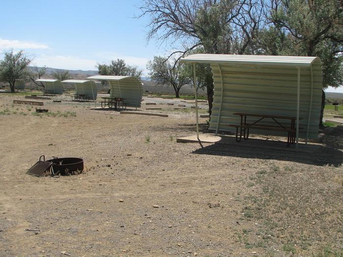 This site has a partially covered picnic table on a slab of cement and a fire pit found in the gravel. There are a number of other sites in the background.Buckboard Crossing Campground: Loop B, Site 25
