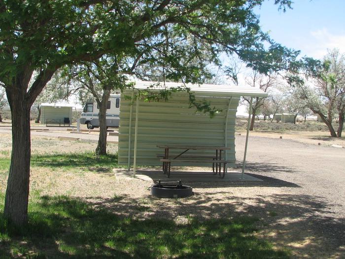 This site has a partially covered picnic table on a slab of cement and a fire pit found in the gravel and has some shade available.Buckboard Crossing Campground: Loop A, Site 27