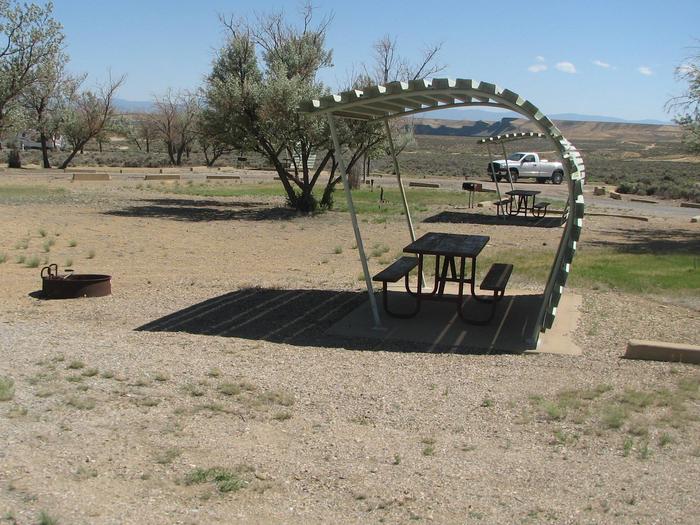 This site has a partially covered picnic table on a slab of cement and a fire pit found in the gravel.Buckboard Crossing Campground: Loop B, Site 31