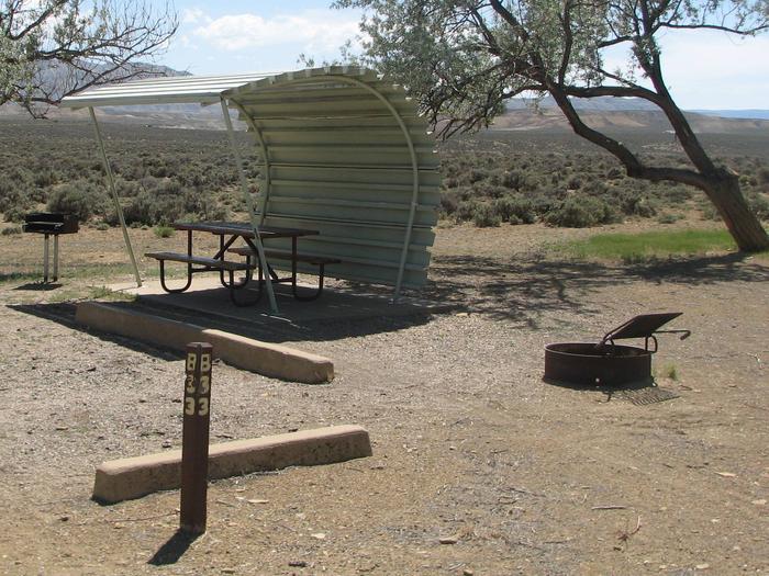 This site has a partially covered picnic table on a slab of cement with a grill next to it held up by a metal rod in the ground and a fire pit found in the gravel. Some shade can be found in this site.Buckboard Crossing Campground: Loop B, Site 33