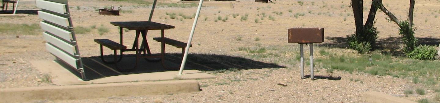 This site has a partially covered picnic table on a slab of cement with a grill next to it held up by a metal rod in the ground. Some shade can be found in this site.Buckboard Crossing Campground: Loop B, Site 34