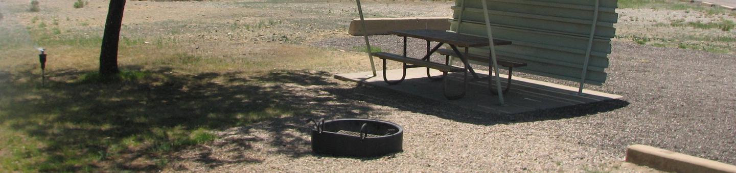 This site has a partially covered picnic table on a slab of cement and a fire pit found in the gravel.Buckboard Crossing Campground: Loop A, Site 7