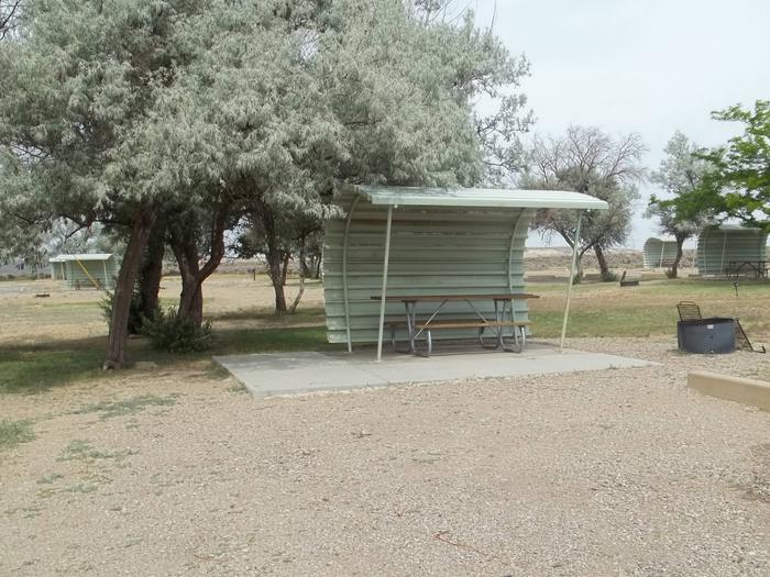 This site has a partially covered picnic table on a slab of cement and a fire pit found in the gravel. There area couple of shade trees in this site.Buckboard Crossing Campground: Loop B, Site 8
