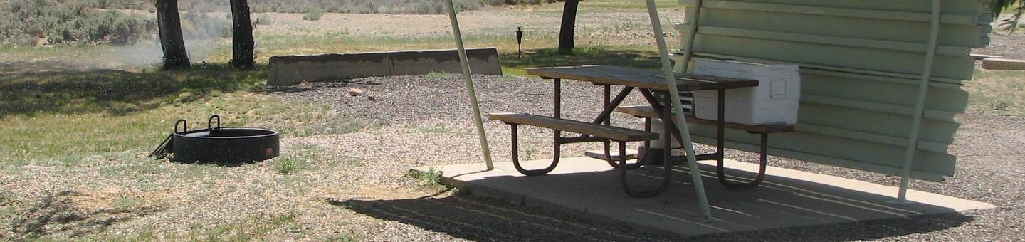 This site has a partially covered picnic table on a slab of cement and a fire pit found in the gravel.Buckboard Crossing Campground: Loop A, Site 9