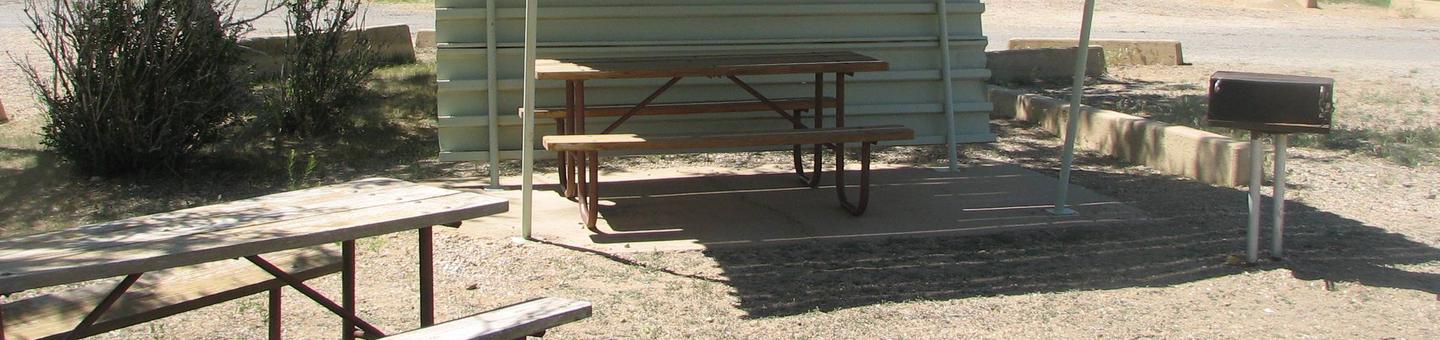 This site has two picnic tables, one of which is partially covered. There is a grill located in a gravel area.Buckboard Crossing Campground, Loop B, Site 9