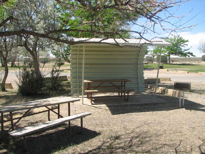 This site has two picnic tables, one of which is partially covered. There is a grill located in a gravel area.Buckboard Crossing Campground, Loop B, Site 9