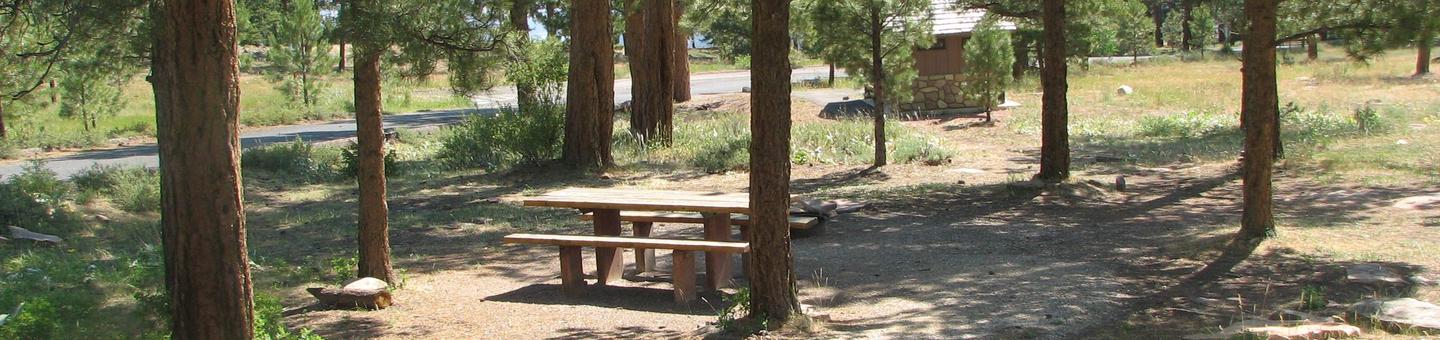 This site has a picnic table and a fire pit that is located in a wooded area. The restrooms can be seen in the background.Canyon Rim Campground: Site 6