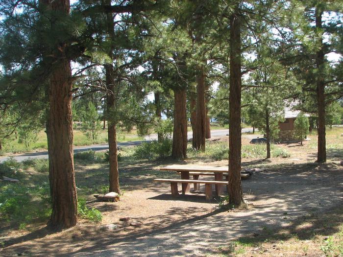 This site has a picnic table and a fire pit that is located in a wooded area. The restrooms can be seen in the background.Canyon Rim Campground: Site 6