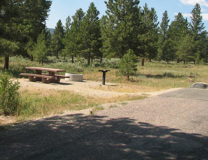 This site has a picnic table and a fire pit in a gravel area to the side of the parking area. Trees and grasses surround the area.Canyon Rim Campground: Site 15