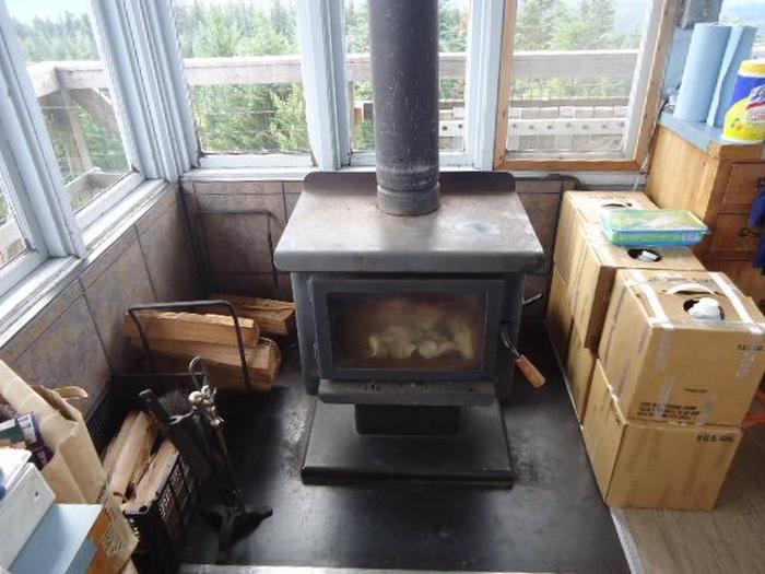 Wood stove next to window filled corner with water jugs and firewood nearby.Clear Lake Cabin Lookout wood stove.