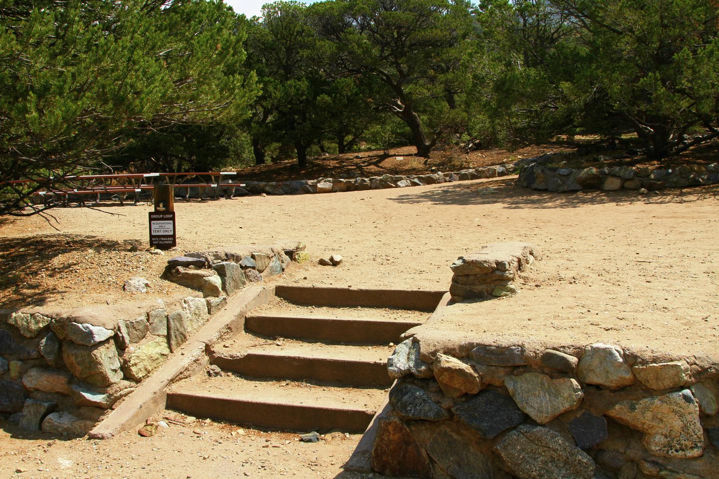 View of Group Site "B" tent area, showing stairs up from parking area to site. Picnic tables can be seen in the background.Group Site B, Pinon Flats Campground