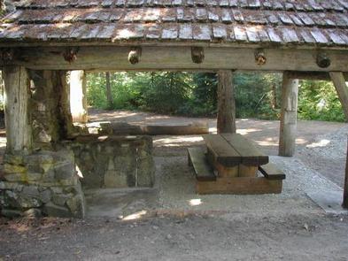 Cascadian style pole shelter protecting picnic table next to stone fireplace and chimney.SILVER FALLS GROUP SITE