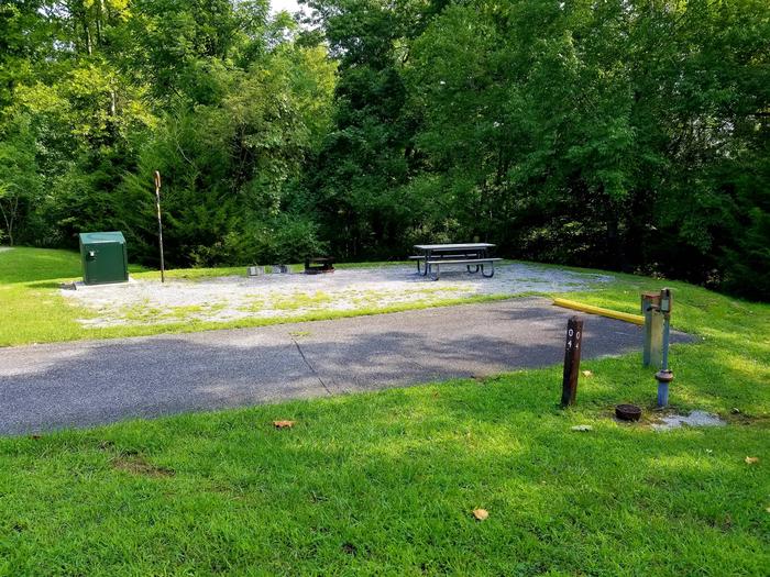 Picnic table sits on gravel tent pad in background of a paved parking spotBlue Heron Campground Site 4