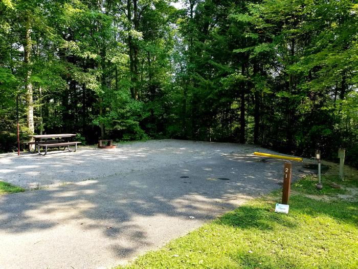 Paved parking spot next to gravel tent pad with picnic table and fire ring.Blue Heron Campground Site 21