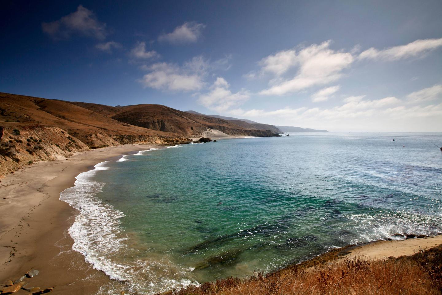 Sandy beach with ocean and small waves and steep coastal bluffs covered in grass. Southeast coast of Santa Rosa Island.