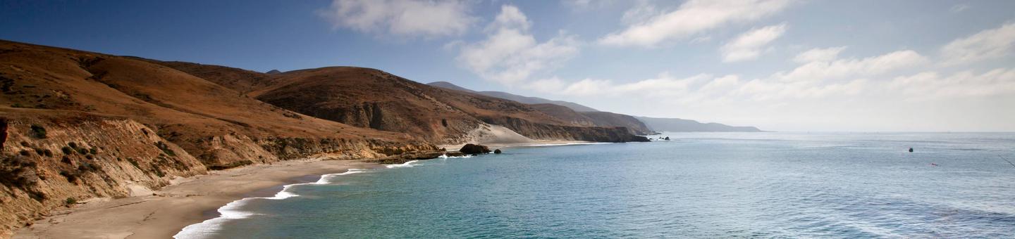 Sandy beach with ocean and small waves and steep coastal bluffs covered in dry grassSoutheast coast of Santa Rosa Island.