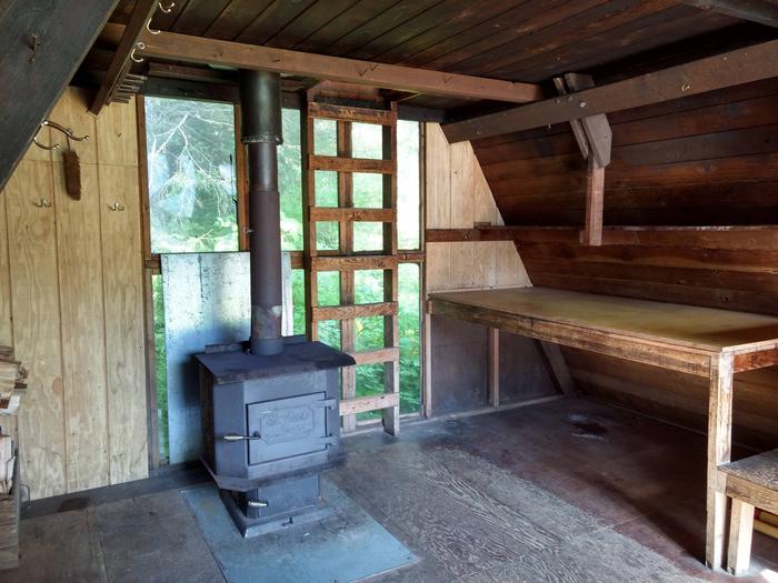 Interior of cabinInterior of cabin with wood stove and showing table along side wall.