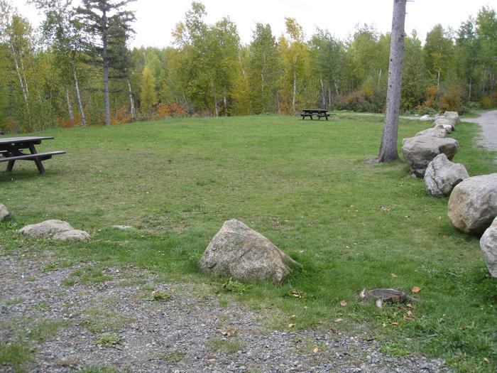 Picture of open grassy area.Group site tent and picnic area with tables and fire grill.  Two gravel parking spurs on each side of the open area.