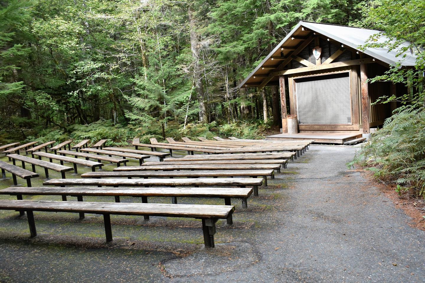 Rustic amphitheater in campground with benches and a building with a stage. Amphitheater located in the campground for ranger programs