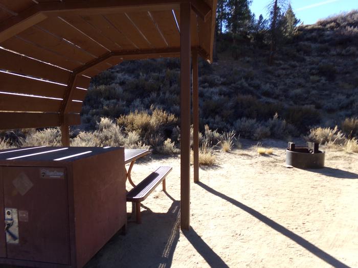 Tuff Campground site #15 featuring shaded picnic area with camping space and fire pit by the mountain side. 