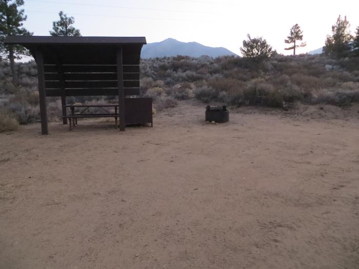 Tuff Campground site #24 featuring the shaded picnic area with camping space and fire pit by the mountain side. 
