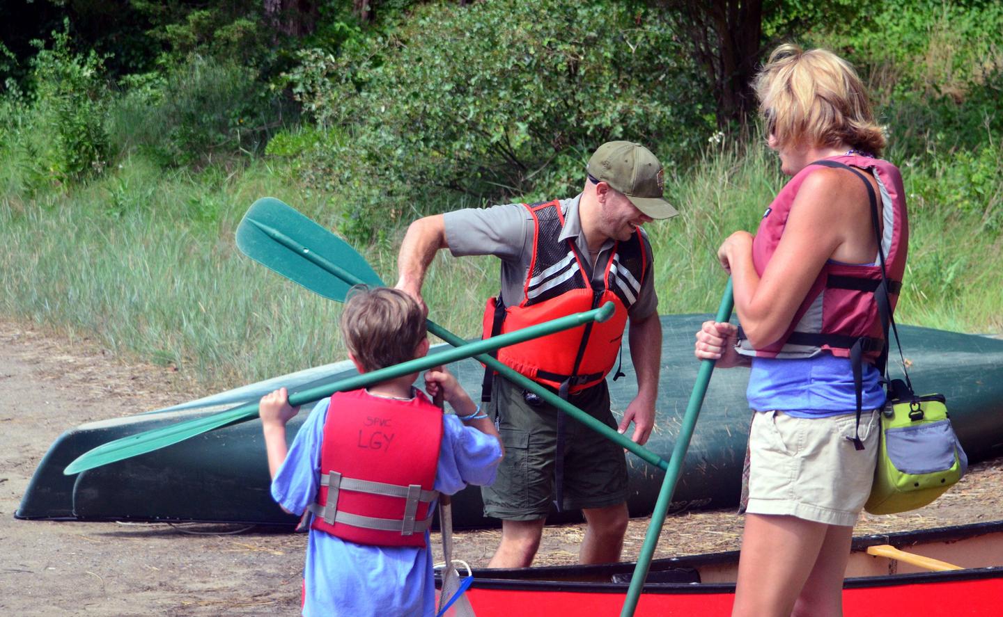 A ranger prepares a canoe for launch while a mother and son look on.