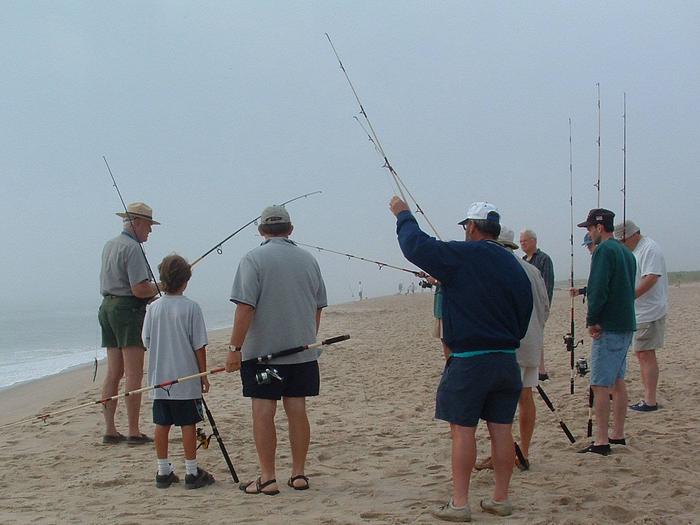 A ranger helps visitors on the beach getting fishing poles ready.