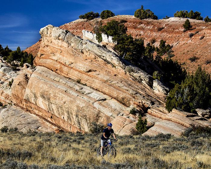Wyoming Johnny Behind the RocksA mountain biker rides his bike in front of a red rock formation. 