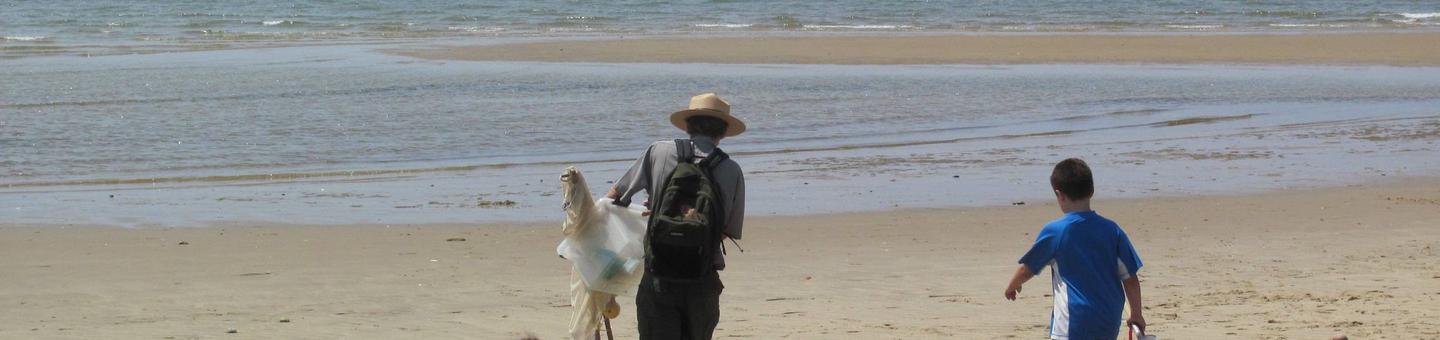 A ranger and a young boy walk out onto the beach carrying nets, and clear plastic bins.
