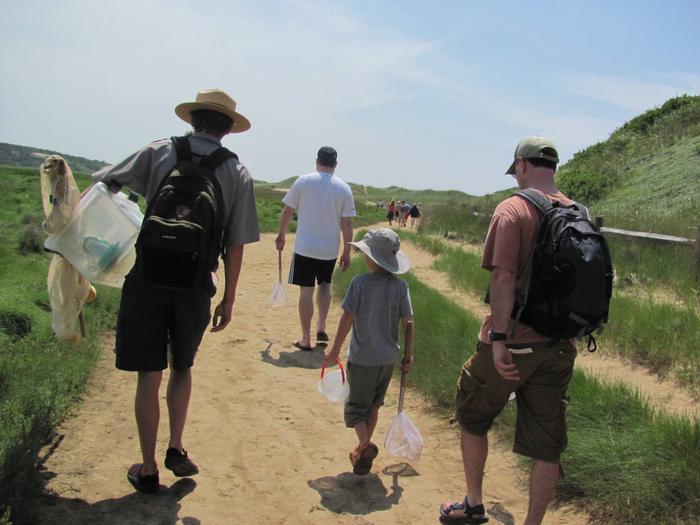 A ranger walks down a sandy path to the beach with a group of people.