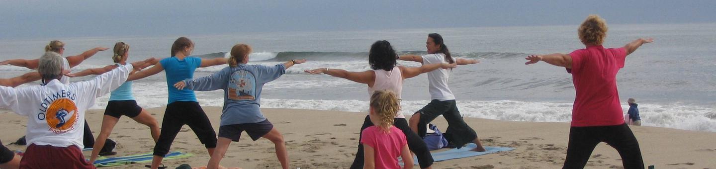 A ranger leads a group doing yoga on the beach.
