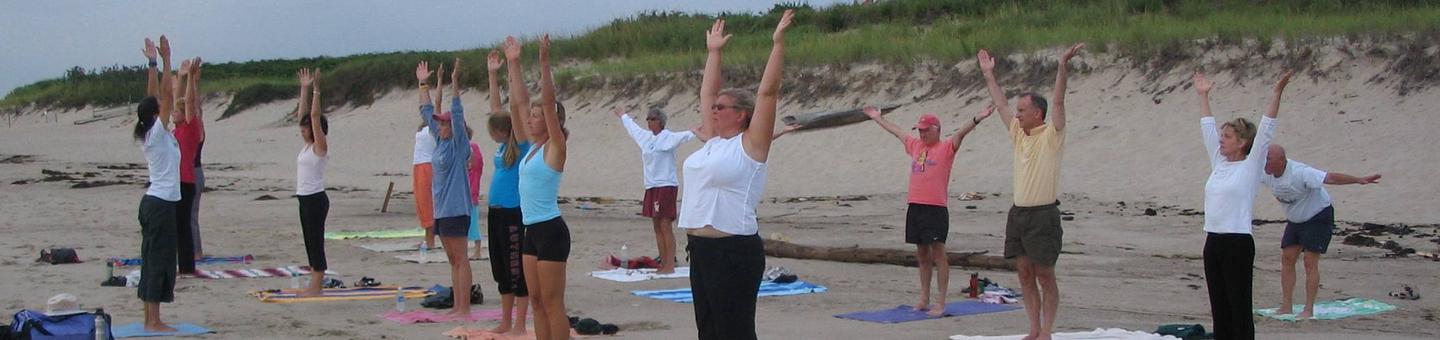 A ranger leads a group of people doing yoga on the beach.