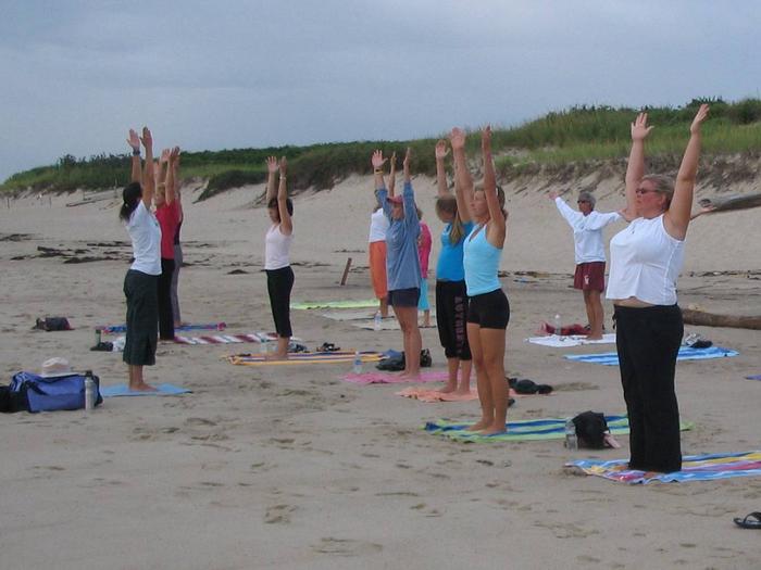 A ranger leads a group of people doing yoga on the beach.