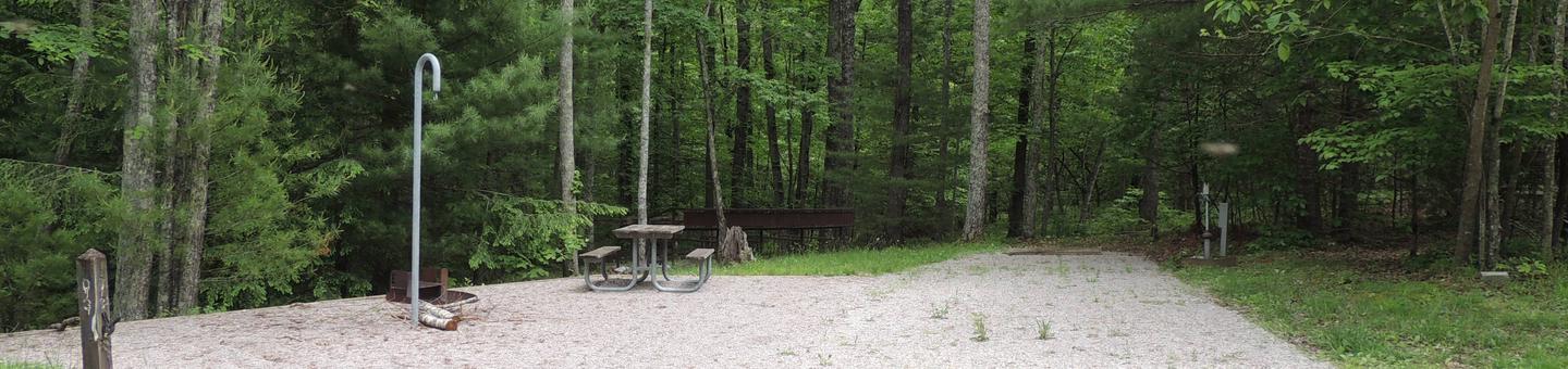 Rocky parking and tent pads with picnic table and lantern hook nearby surrounded by green treesSite 3