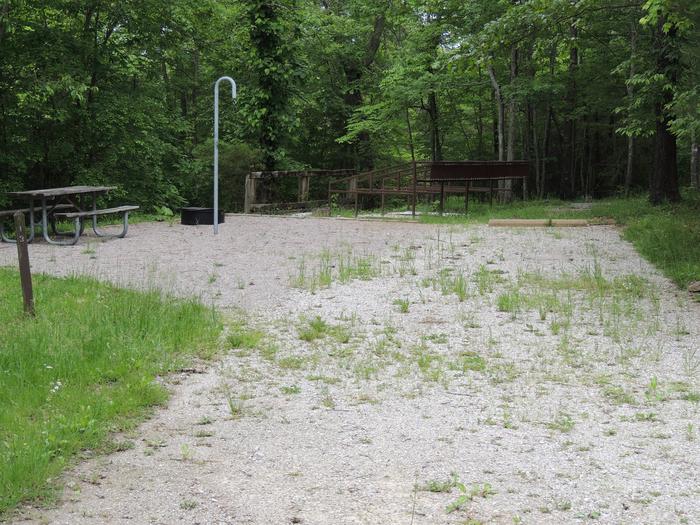 Gravel parking alongside tent pad with picnic table and lantern hook. Green trees surround the site.Site 13