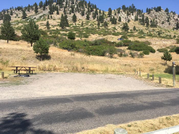 Site 32 BLM Holter Lake Campground. Paved access to campsite. Graveled campsite with picnic table and fire pit. Trees and shrubs above campsite. Campsite is below Beartooth Road.Site 32 BLM Holter Lake Campground.