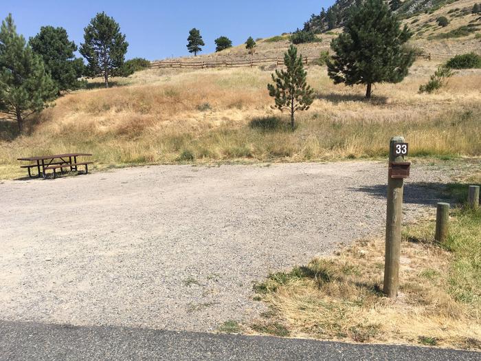 Site 33 BLM Holter Lake Campground. Paved access to campsite. Graveled campsite with picnic table and fire pit. Trees, shrubs and Beartooth Road above campsite.Site 33 BLM Holter Lake Campground