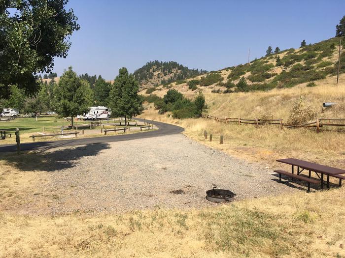 View of Holter Lake Campground from site 22. Paved access leads to graveled pad with picnic table and fire pit.Site 22 BLM Holter Lake Campground