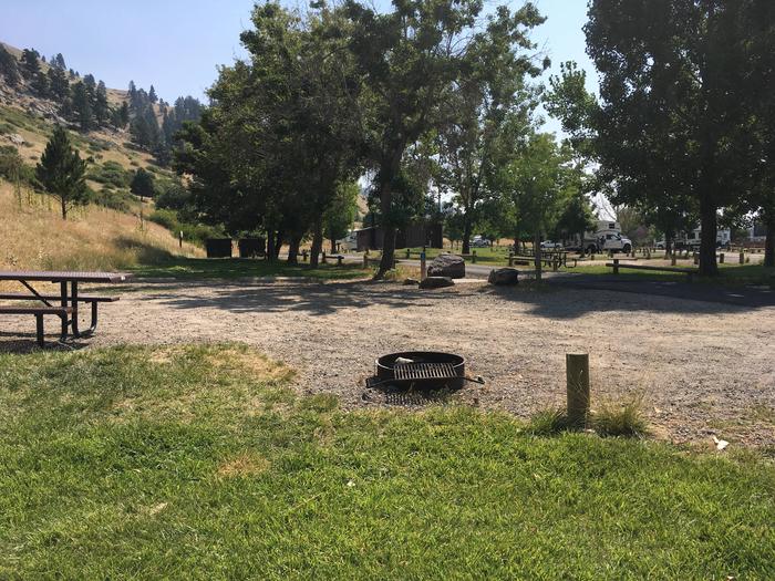 Site 27 BLM Holter Lake Campground. Fire pit and picnic table in the foreground where the graveled campsite meets with the grass. Potable water available but no hook-ups throughout campground. Containers must be filled.Site 27 BLM Holter Lake Campground