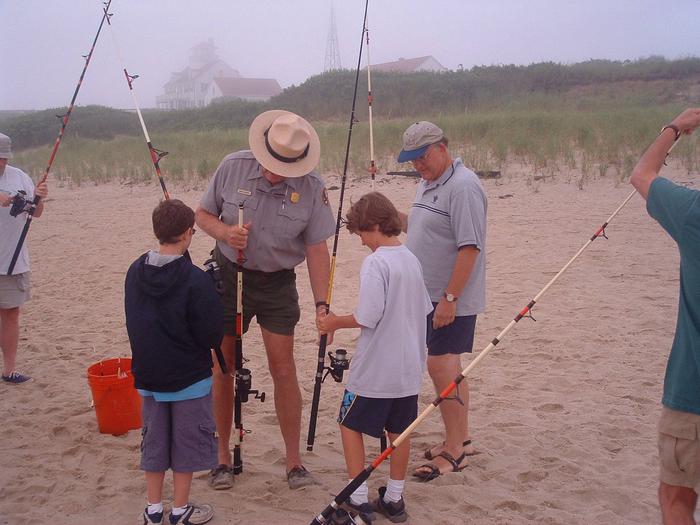 A ranger on the beach helps two young boys rigging up fishing gear.