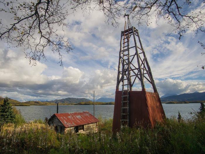 View of a wood cabin and windmill in a grassy field with a lake and mountains in the background.Fure's Cabin and windmill, located in the Bay of Islands, Naknek Lake. Fure's Cabin is not a substitute for the Brooks Camp campground and is located a full day's paddle away.