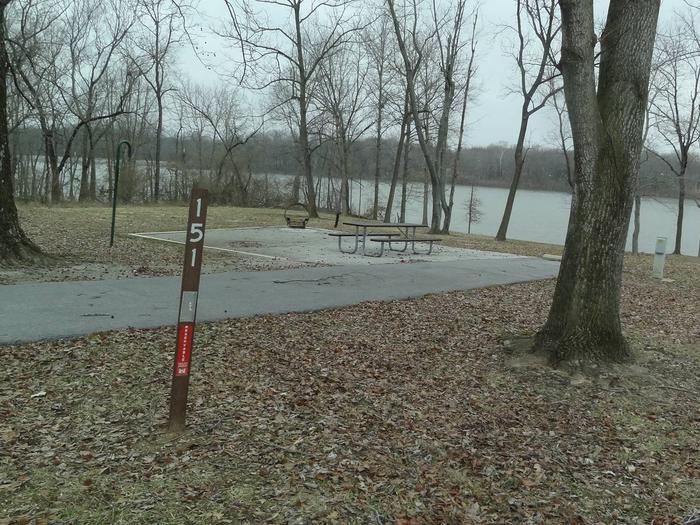 picnic table and fire pit to the left of camp pad, electric and water to the right of pad.