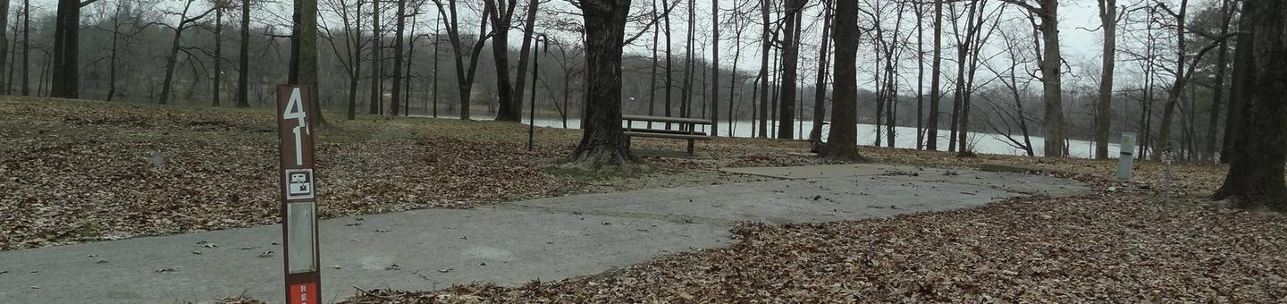 picnic table and fire pit to the left of camp pad, electric, water, and sewer to the right of pad.