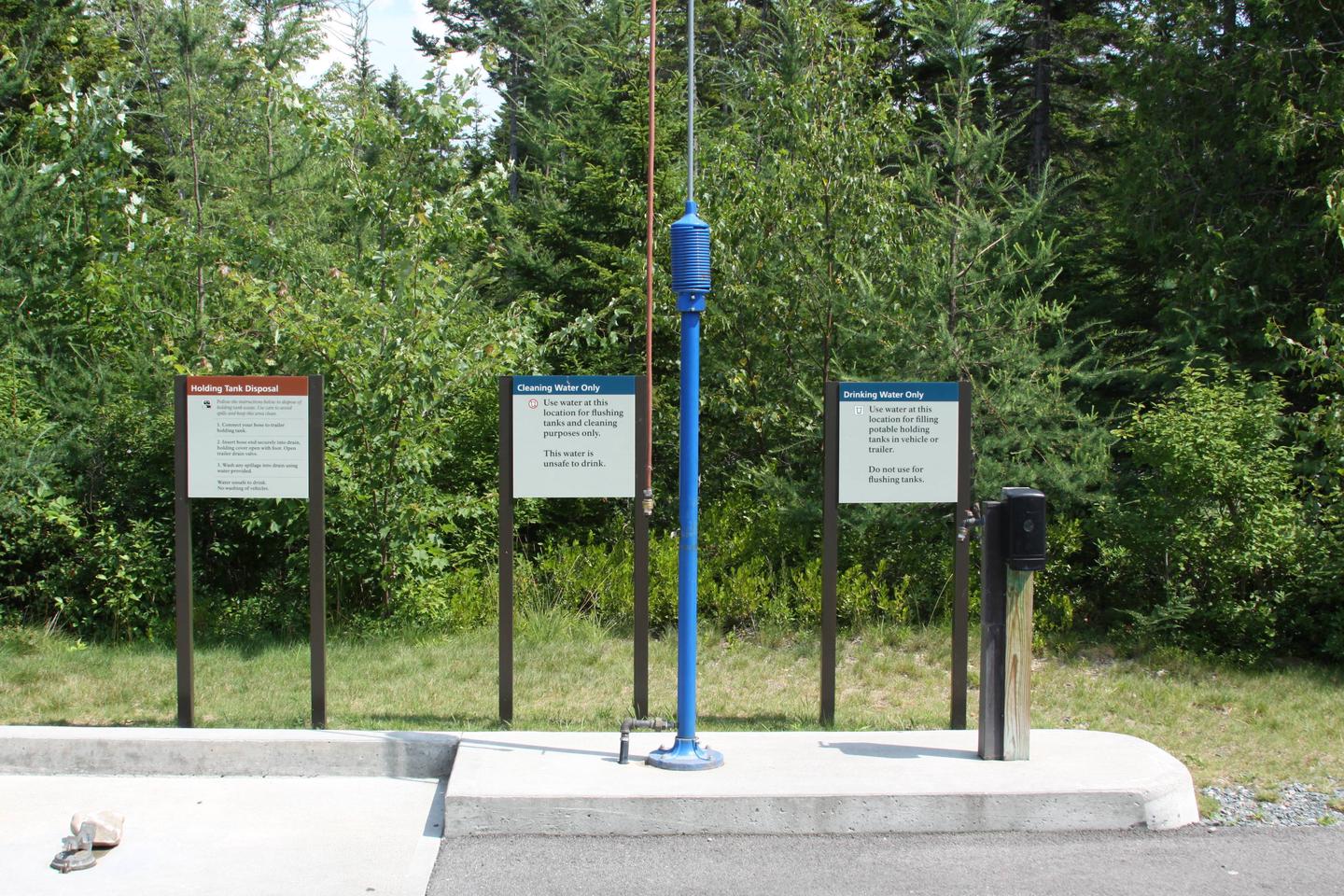 A series of three signs showing area for dumping waste, cleaning water, and drinking water with green shrubs in background.Dump station, cleaning water, and drinking water