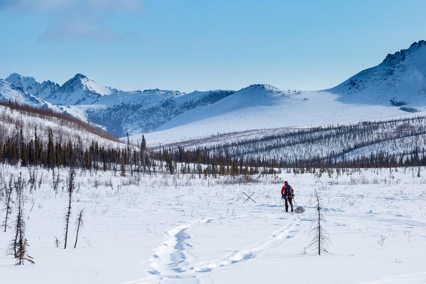 A skier pulling a sled follows a trail through snowy mountains.