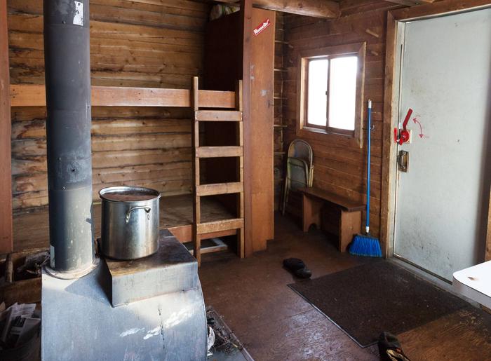 Inside of log cabin with bunks, window, and woodstoveInterior of Colorado Creek Cabin with woodstove and bunks.