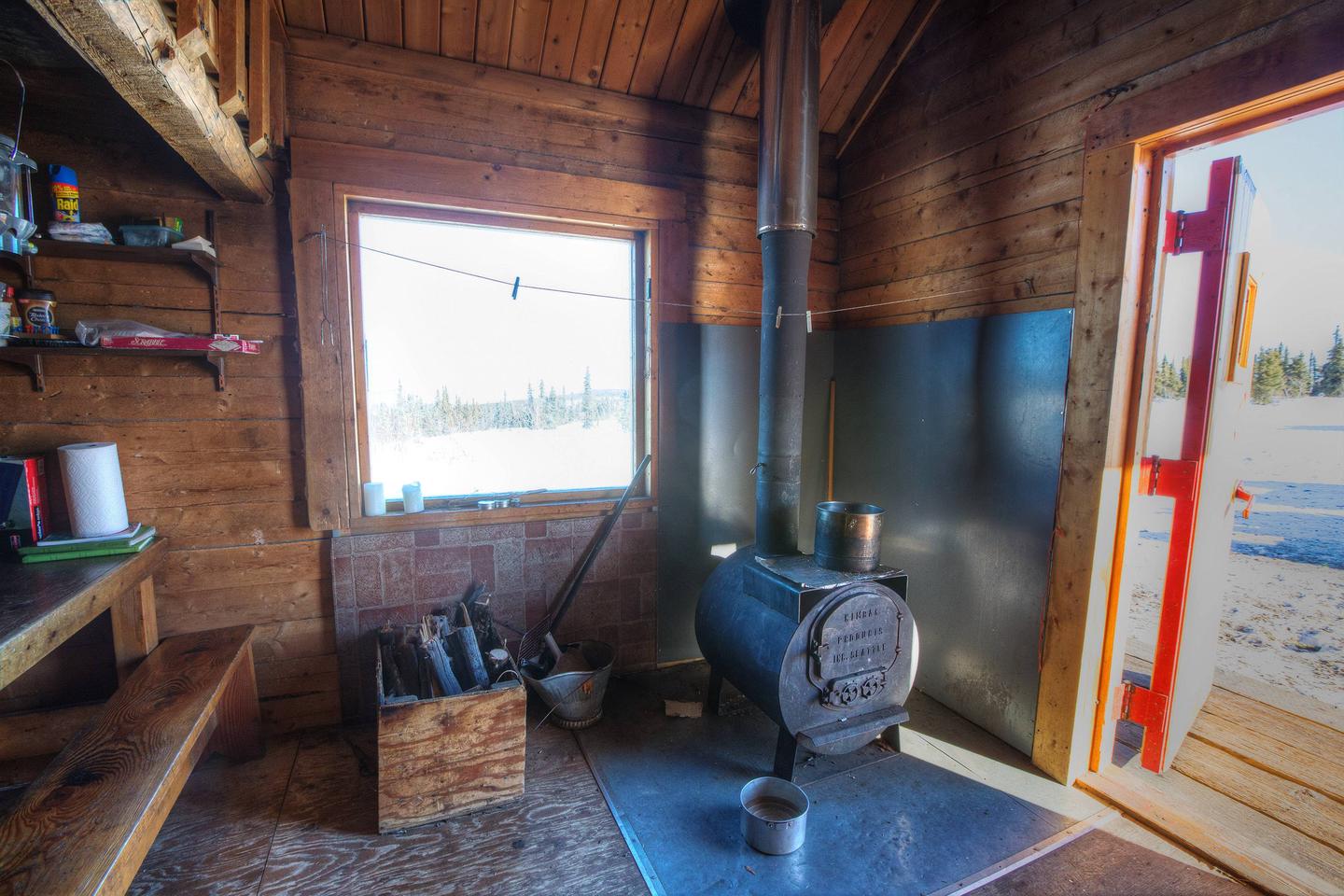 Inside view of log cabin with woodstove, window, and doorwayWoodstove and picture window at Lee's Cabin