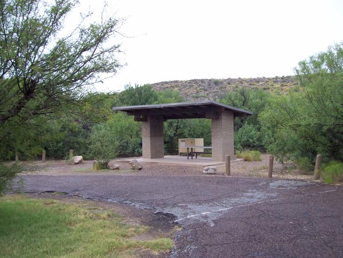 A paved road leads to an open shade and shelter. Beneath the shelter is a picnic table, metal grill, and bear box. The paved roadway is a pull-through parking space with a tight arc, and is not recommended for longer RVs.Tight arc for a parking space
