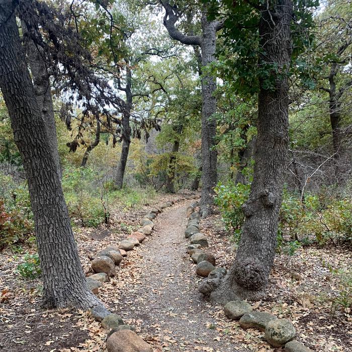 Stones lines the edges of a trail through the woods inviting exploration.Stones line the edges of the Quanah Parker Lake Trail which leads from Doris Campground to the Environmental Education Complex and includes an accessible fishing pier.