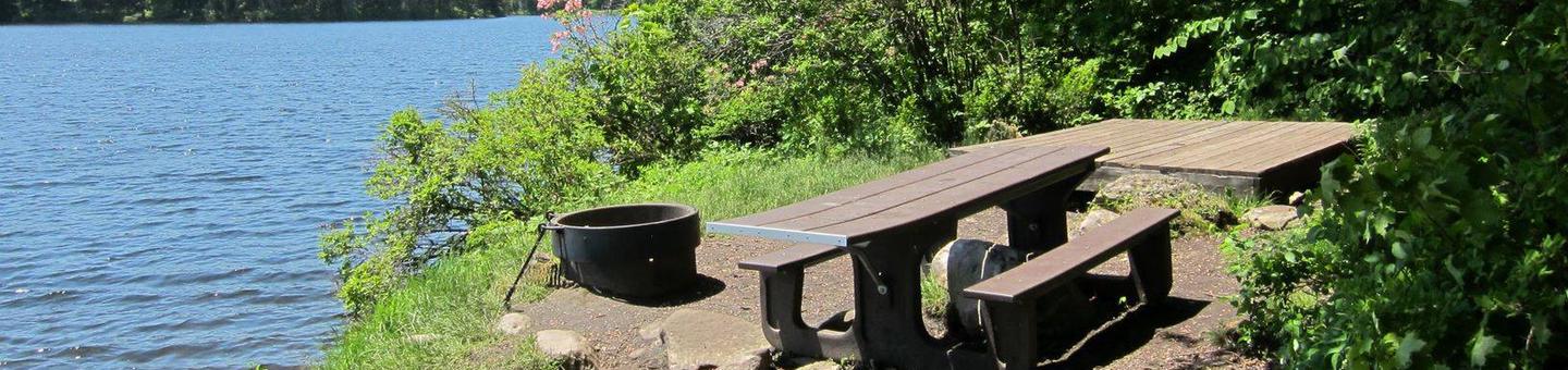 picnic table, fire ring, and tent pad in the foreground, pond in the backgroundcampsite 7